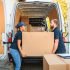 Delivery team of man and woman lifting a giant cardboard box towards the storage space of the van.