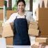 Young woman owner of online business and small courier, standing with box in office smiling proudly, parcel delivery, e-commerce.